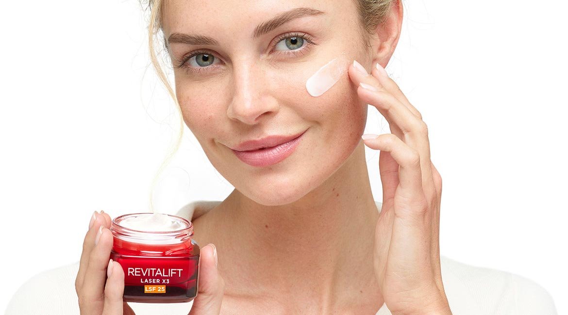 Eine Frau trägt eine Creme aus einem Tiegel auf ihre Wange auf